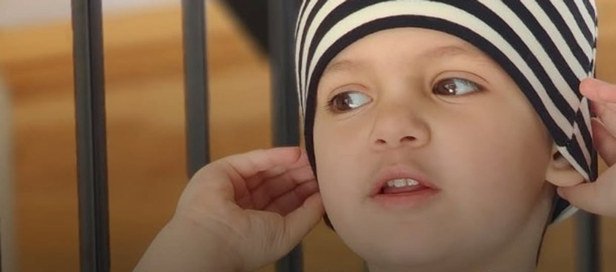 Léon, enfant soutenu par Leucan, ajuste sa tuque rayée noir et blanc, les mains près des oreilles.